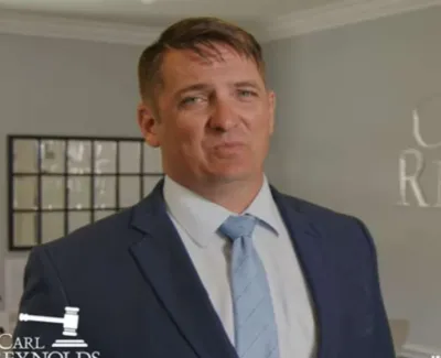 Professional man in blue suit and tie stands in front of Carl Reynolds Law office wall with gavel logo.