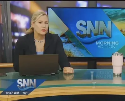 Two news anchors presenting the SNN Morning Edition with laptops and a cup on the desk in a studio.