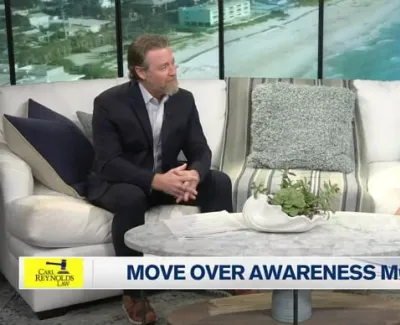 Two hosts discussing Move Over Awareness Month on a TV set with beach view backdrop and white couches.