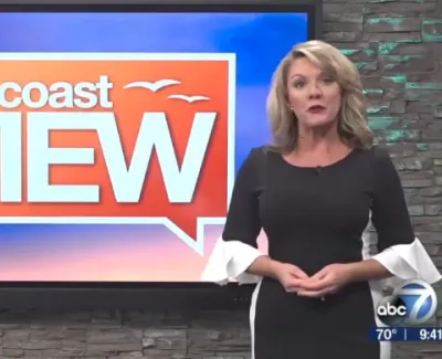 Female news anchor standing beside Suncoast View show logo on TV screen in studio setting
