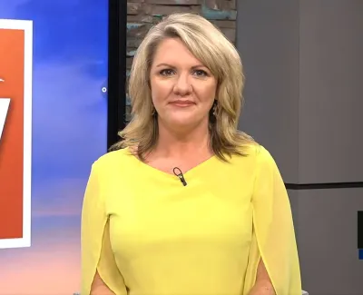 News anchor in yellow top delivering broadcast with Your Local Station logo and time 9:14 displayed