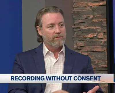 Man in a navy blazer discusses legal topic on recording without consent in TV studio setting.
