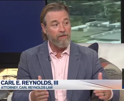 Attorney Carl E. Reynolds III speaking during a televised interview in a studio setting.