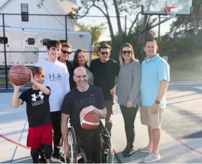 Group of diverse people including a man in wheelchair holding basketballs on an outdoor court in sunny weather