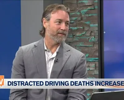 Man in gray suit discussing rise in distracted driving deaths on a TV news show set.