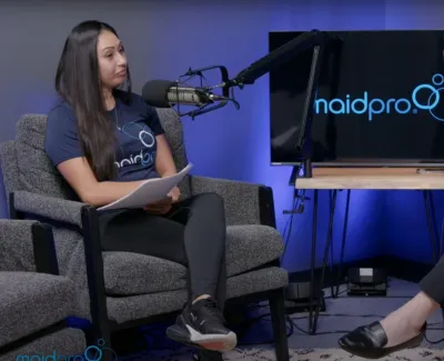 Two women seated in a podcast studio with microphones, discussing in front of a screen displaying maidpro logo.