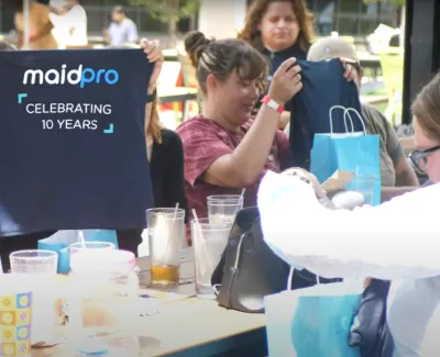 Group of people at outdoor table celebrating MaidPro's 10th anniversary with drinks and gift bags.
