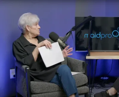 Two women engaged in a podcast interview with MaidPro logo on screen behind them in recording studio.