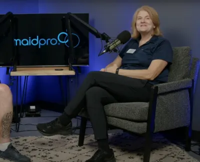 Two people sit in armchairs with microphones, recording a podcast or interview in a studio with MaidPro branding.