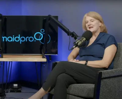 Two women speaking into microphones during a MaidPro podcast recording with MaidPro logo on screen behind them