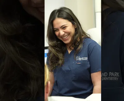 Smiling female dentist in navy scrubs interacting with a patient in a modern dental office.