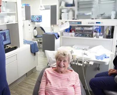Smiling elderly woman sitting in a dental chair talking with a male dentist in a bright dental office.