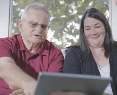 Three people sitting indoors engaged in a discussion while looking at a tablet screen together.
