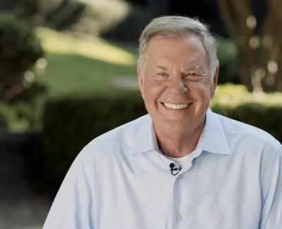 Smiling elderly man in white shirt outdoors with blurred greenery background on sunny day