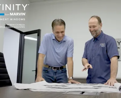 Two men discuss blueprints at a conference table in an office with Infinity from Marvin branding.