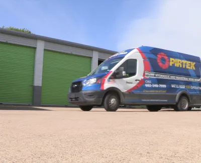 Pirtek service van and trailer parked outside a building with green garage doors on a bright day