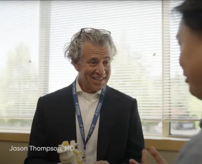 Doctor in suit explaining spine model to patient inside bright medical office with Proliance logo