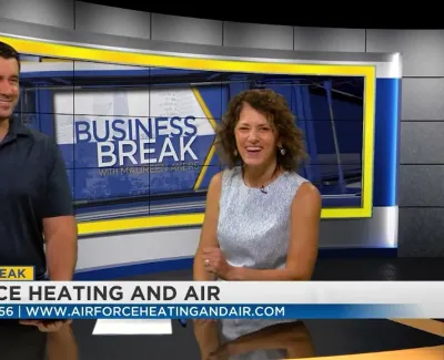 Two hosts smiling on a Business Break TV set with Airforce Heating and Air ad banner and contact info
