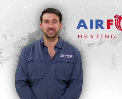 Man in navy uniform standing in front of Air Force Heating and Air logo with wintery background and falling snow.