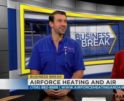 Two hosts discussing Airforce Heating and Air on Business Break TV show set with contact info banner.