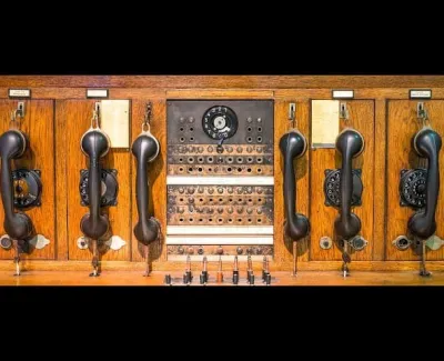 Vintage wooden telephone switchboard with multiple black handsets and rotary dial in the center.