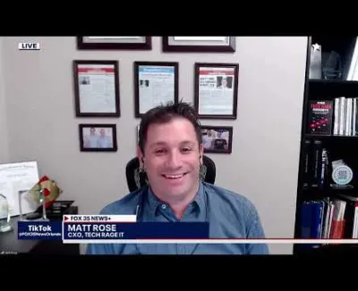 Smiling man in blue shirt speaking during a Fox 35 News+ live interview with certificates and books behind him