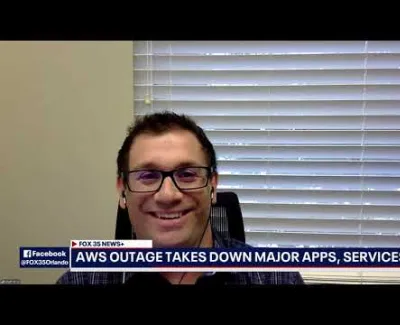 Smiling man wearing glasses and earphones during a news segment about AWS outage affecting major apps and services.