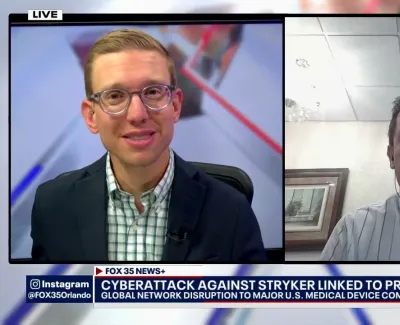 Two men in a live news broadcast discussing cyberattack on medical device company linked to pro-Iranian group.