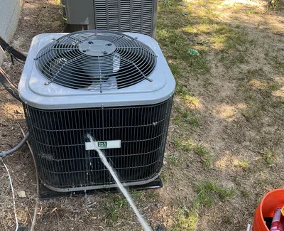 Technician testing outdoor air conditioning unit's efficiency with a digital gauge on a sunny lawn with tools nearby.