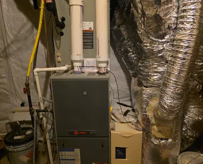Basement HVAC system with Trane furnace, insulated ductwork, and white PVC pipes for ventilation and drainage.