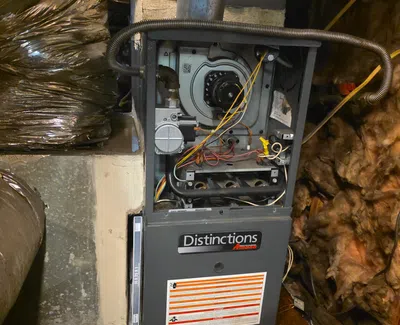 Open Amana Distinctions furnace showing internal components and wiring in a basement with insulation and ductwork.