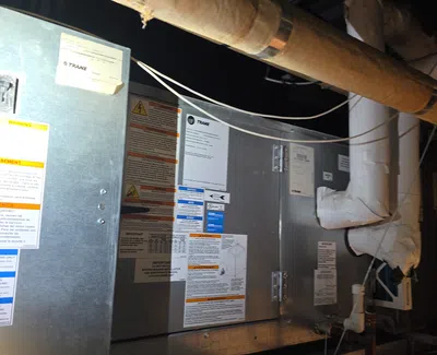 Industrial HVAC unit with ductwork and warning labels in a basement or mechanical room.