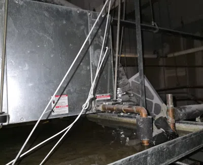 Water pooling inside HVAC unit with visible pipes, wires, and metal framework in industrial setting.