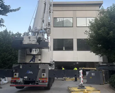 Large Demag crane with extended stabilizers operating in front of a modern office building during daytime.