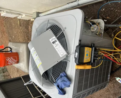 Outdoor HVAC unit undergoing maintenance with diagnostic tools, pressure gauges, and an orange Home Depot bucket.