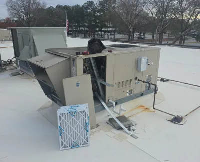 Commercial rooftop HVAC unit with open panel and new air filter ready for installation on white flat roof.