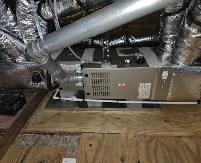 Bryant HVAC unit installed in attic surrounded by insulated ductwork and ventilation pipes.