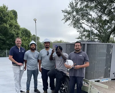 Group of five HVAC technicians posing with equipment on a rooftop under cloudy sky