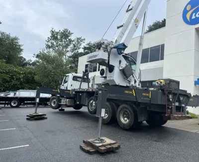 Mobile crane with extended stabilizers parked outside an office building on asphalt parking lot.