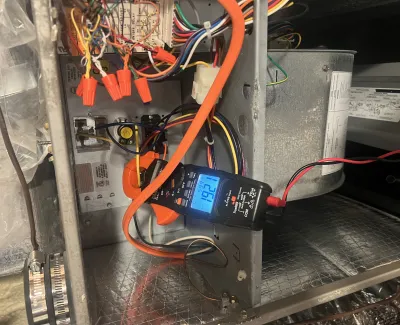 Digital clamp meter measuring current inside HVAC unit with visible colored wires and metal components.