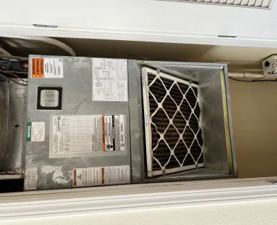 HVAC air conditioning unit with visible air filter and warning labels inside a closet space.