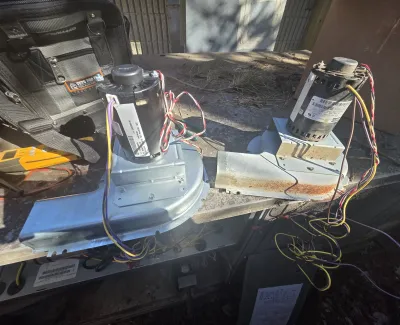 Two HVAC blower motors with wiring resting on a metal workbench in an outdoor setting.