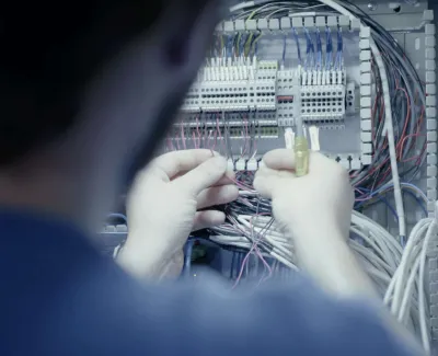 Electrician working on wiring connections inside an electrical control panel with multiple cables and components.