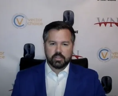 Man in blue suit speaking in front of a branded backdrop with Vector Choice and WN logos