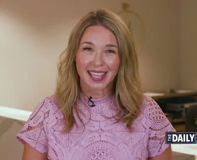 Smiling woman with blonde hair in pink lace top presenting news in a modern studio setting