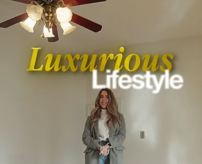Woman in stylish coat and jeans standing in empty room with wooden floor and ceiling fan under luxurious lifestyle text.