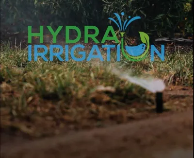 Lawn sprinkler watering grass in a garden with Hydra Irrigation logo and residential service sign in background