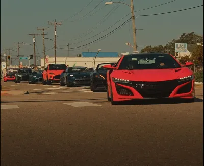 Line of luxury sports cars stopped at a green traffic light on a clear day with power lines overhead.