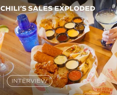 Chili’s table spread with fried chicken, fries, sauces, and margaritas with hands holding drinks at wooden table.