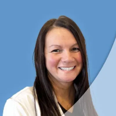 Smiling woman with long brown hair wearing a white coat against a blue background with curved design.